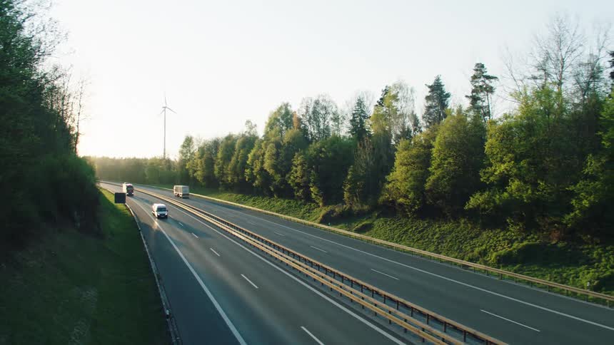 Several cars and trucks are driving down a highway that is lined by trees