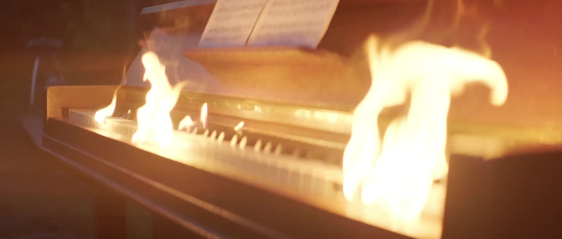 A piano with its keys on fire and sheet music on its stand