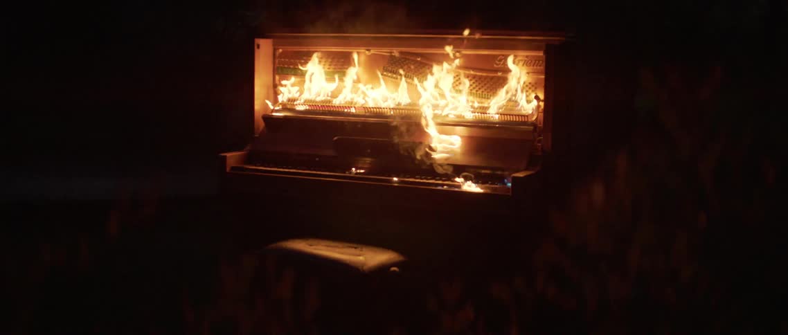 Upright piano set on fire burning at night outdoors