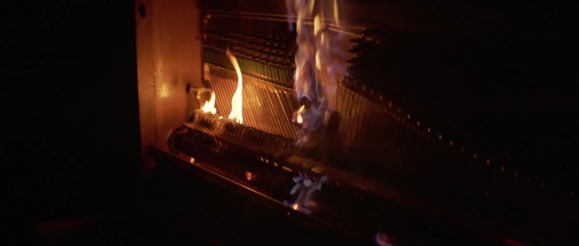 A fire burns up a piano in the dark