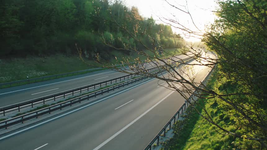 Vehicles drive down a divided highway surrounded by trees