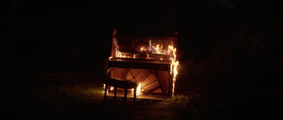 Upright piano engulfed in flames on a lawn at night