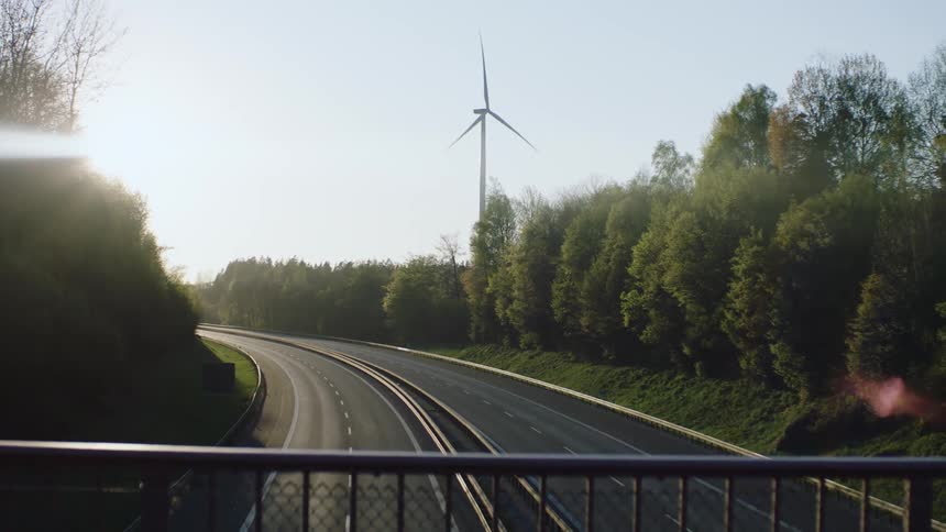 A wind turbine turns on the side of an empty highway with an overpass