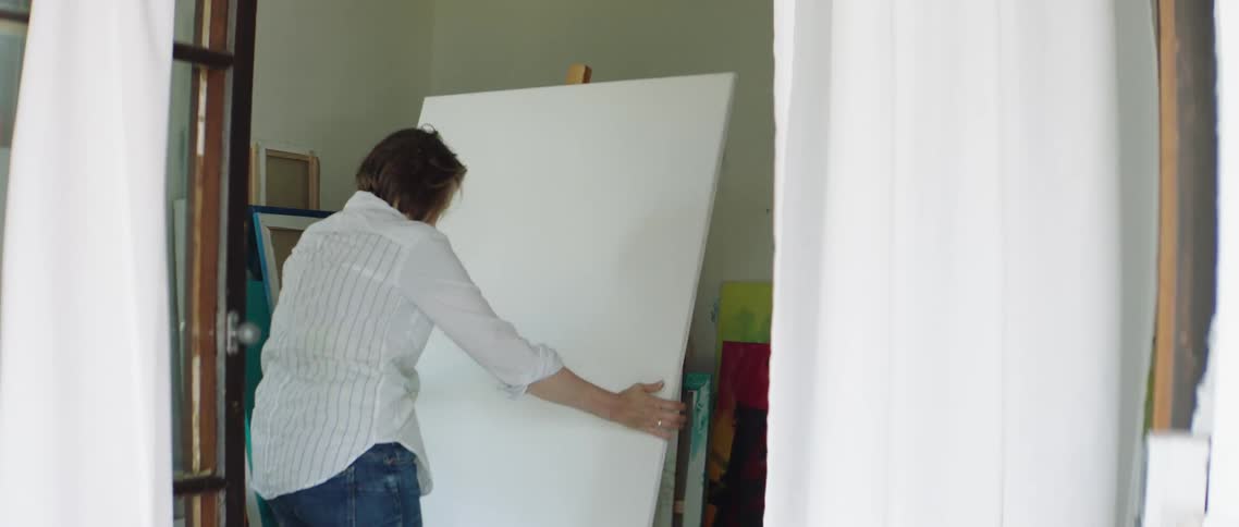 Woman places large canvas on easel in art studio