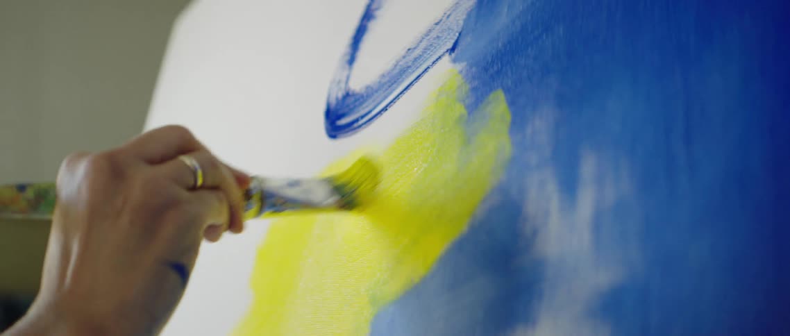 A persons hand holding a paintbrush and painting on a canvas