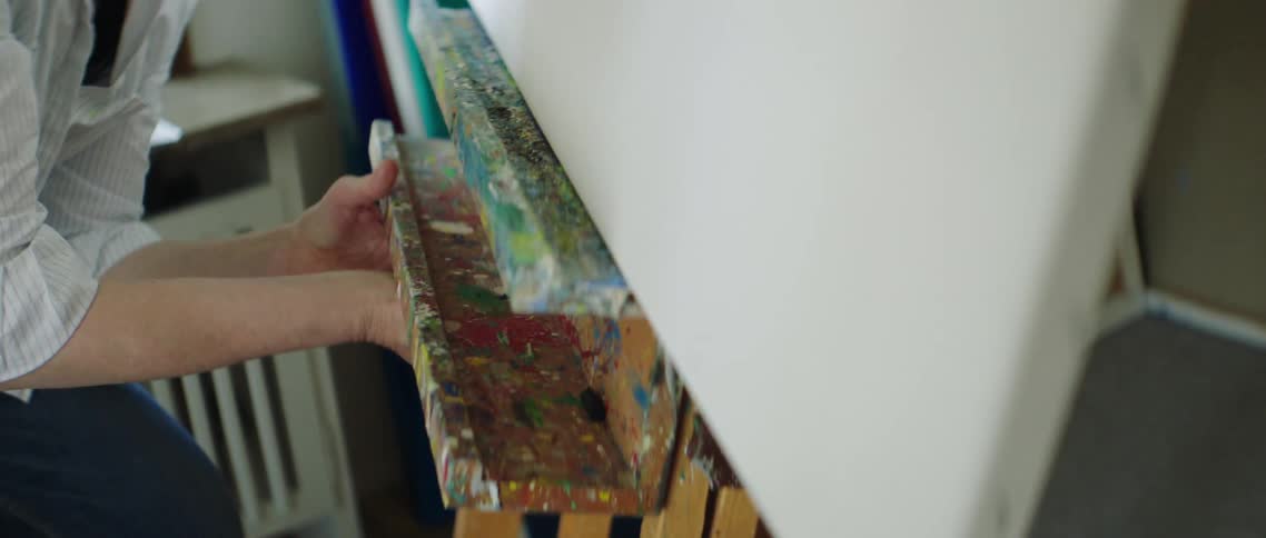 Female lifts up on the tray of the easel with a blank canvas making it taller in height