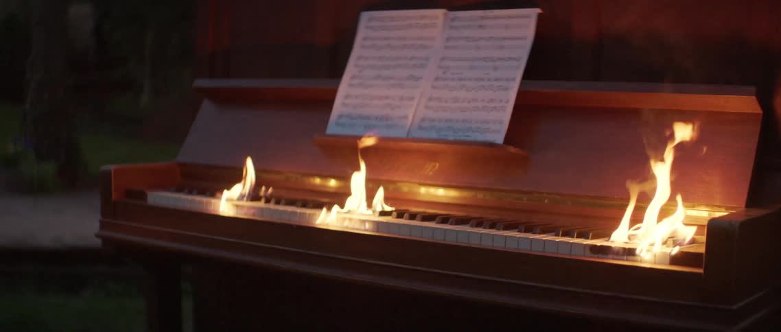 A burning piano outdoors on a grass lawn