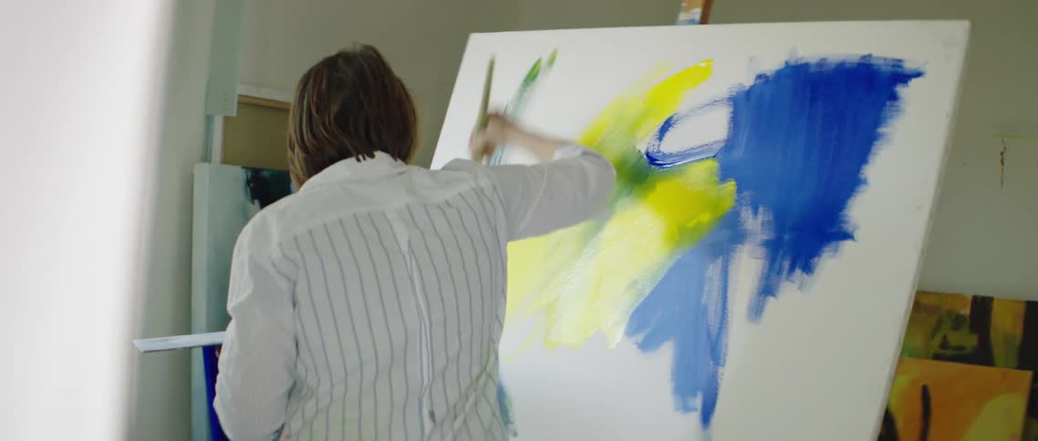 A white woman paints colors on a large canvas