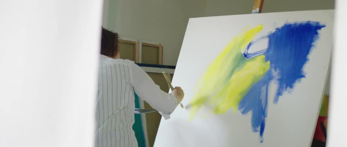 A woman uses a paintbrush to paint a canvas