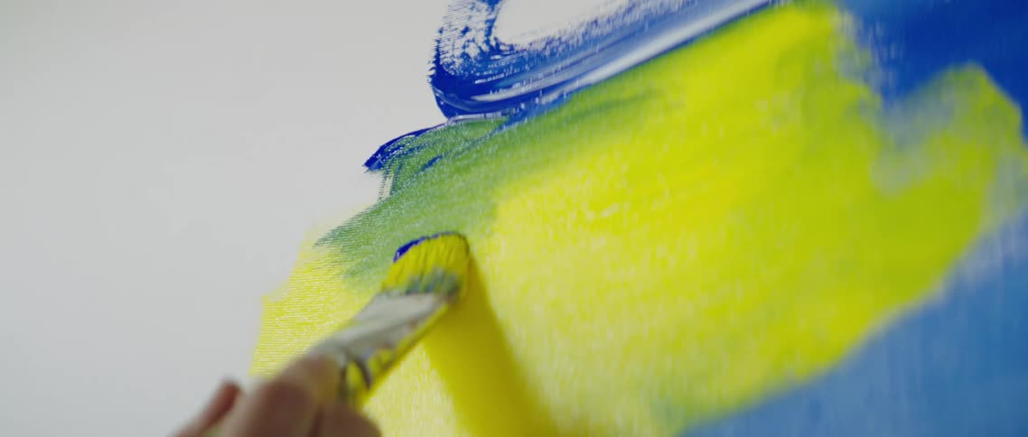 Person painting with yellow and blue paint on canvas