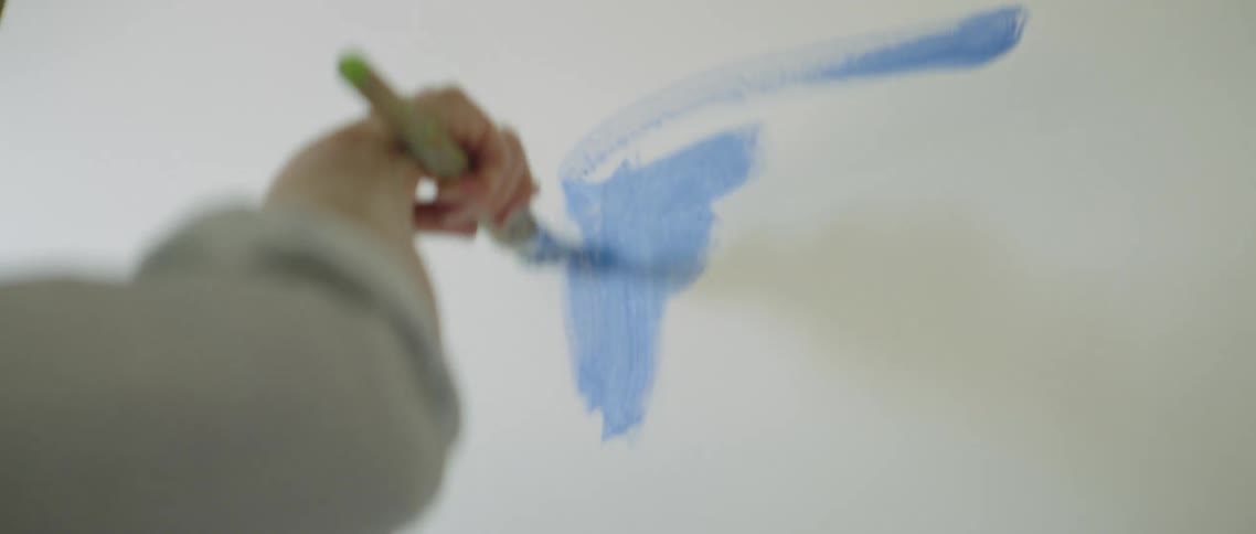 Woman brushes blue paint onto large canvas