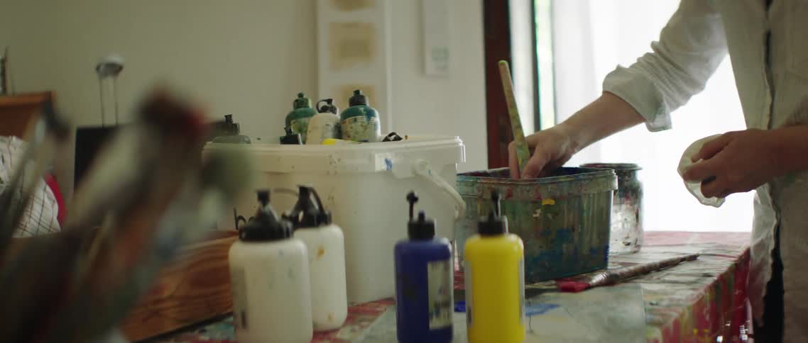 A person uses a paintbrush to mix paint in a large bucket