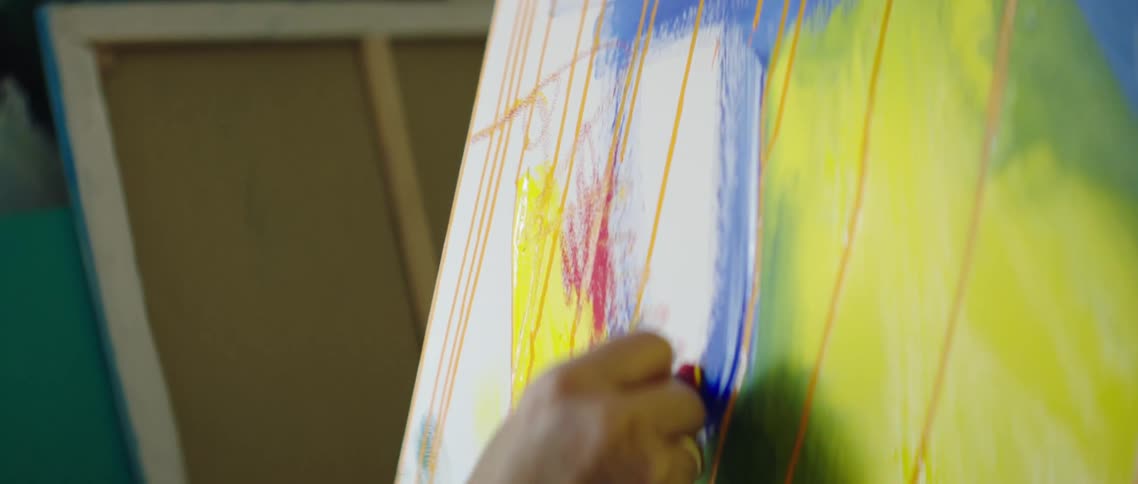 A white woman draws marks on a painted canvas
