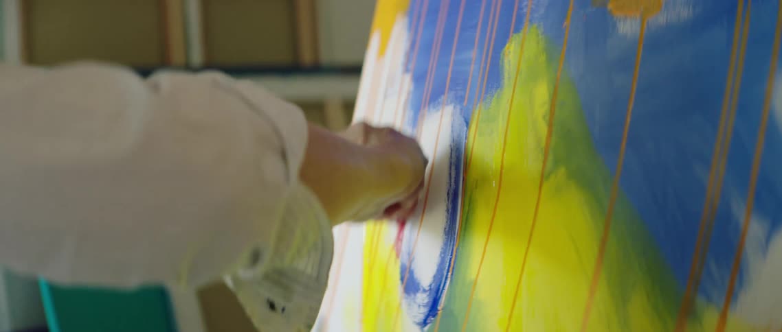 A painter holds a box of colored chalk while painting on canvas inside a studio