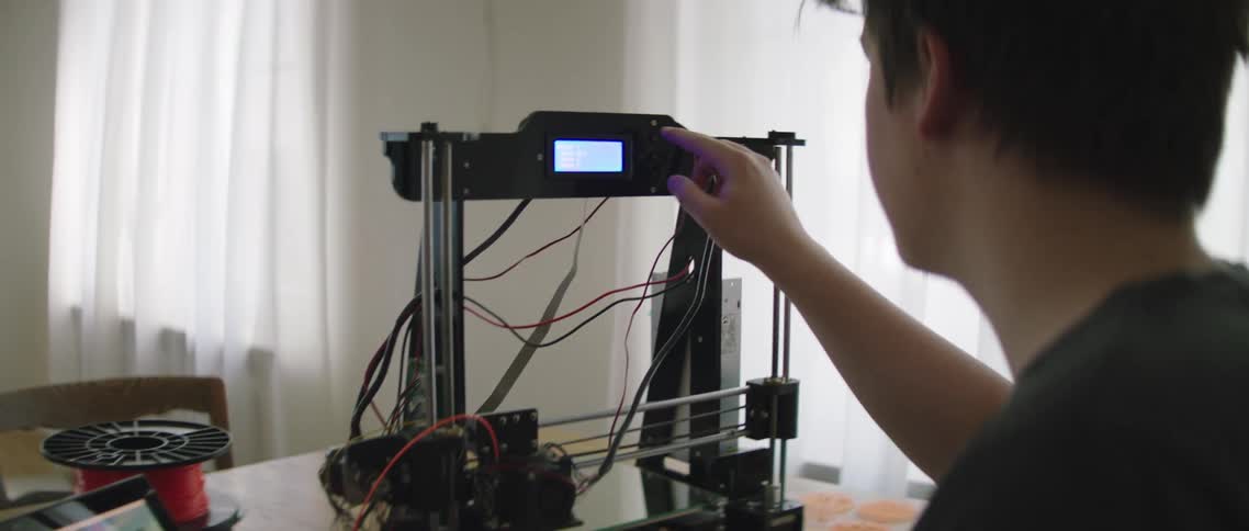 A man in front of a laptop adjusting a 3d printer