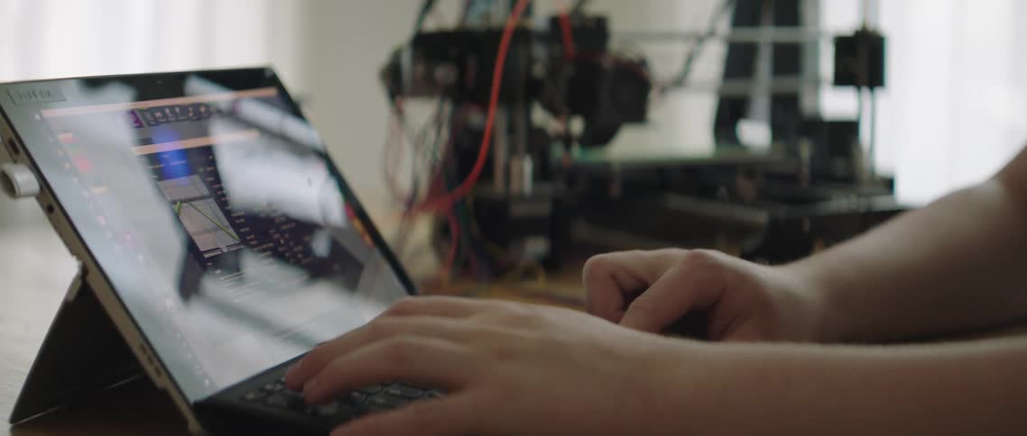 A person types on a laptop sitting on a table beside other machinery