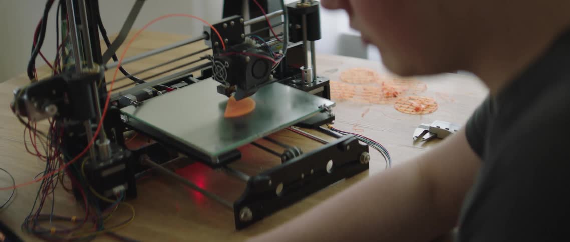 A man works on a laptop while a 3d printer prints