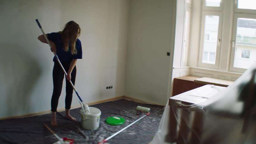 Woman in a room covered in plastic sheets starts painting the walls
