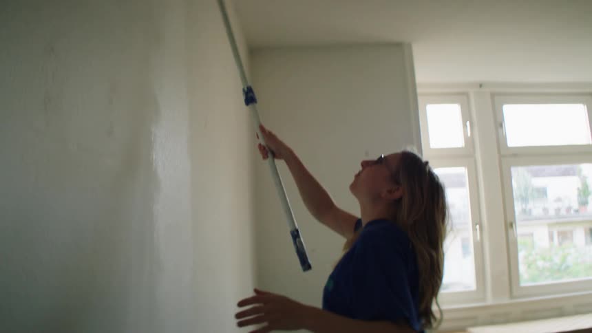 Woman rolls white paint onto wall with paint roller