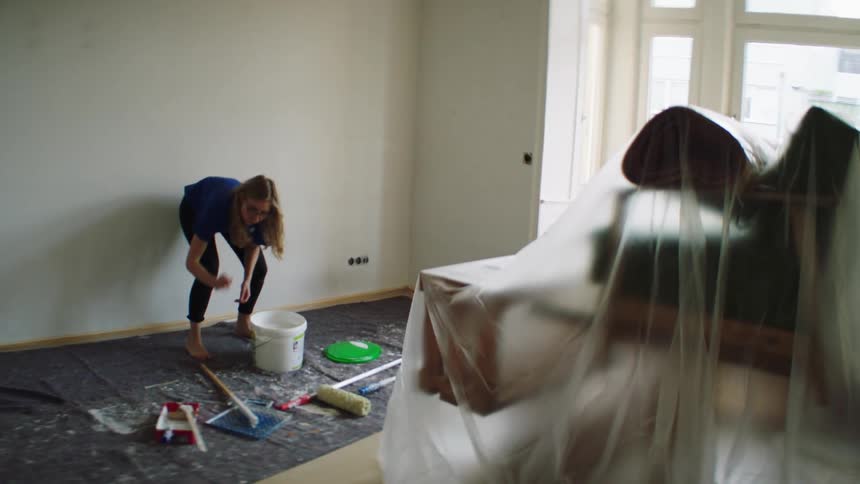 Barefoot woman mixes paint in a bucket to paint a room