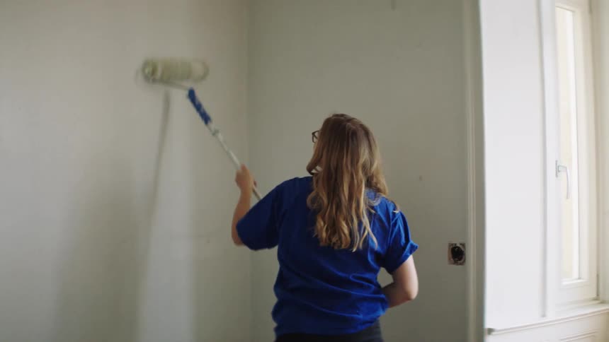 A woman with a paint roller painting a wall