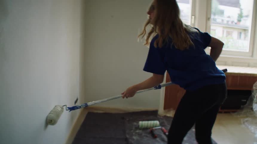 A woman is using a roller to paint her wall