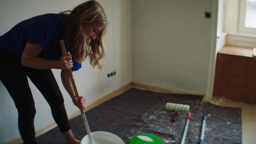 Woman stirs large bucket of latex interior paint