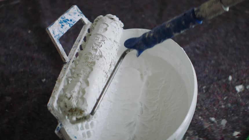 A paint roller being dipped into a bucket of white paint