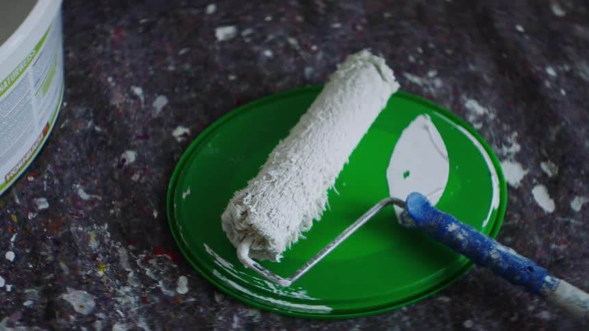 A paint roller is sitting on a bucket lid next to a bucket of paint
