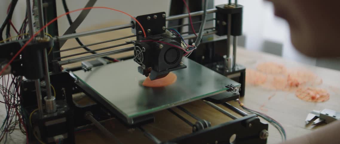 A person sits in front of a laptop and a 3d printer in motion