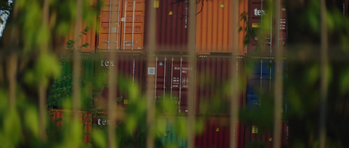 A fence with shipping containers in the background