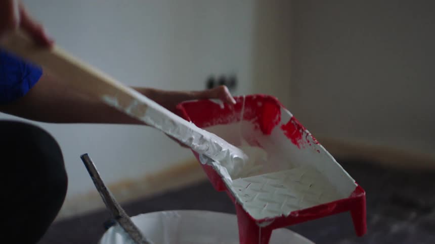 A person uses a wooden stick to place paint into a paint tray