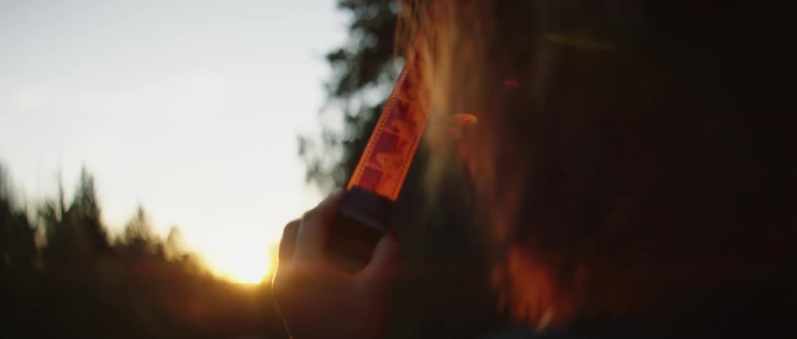 A man goes through a roll of 35 mm film while standing outside at sunset in a forest