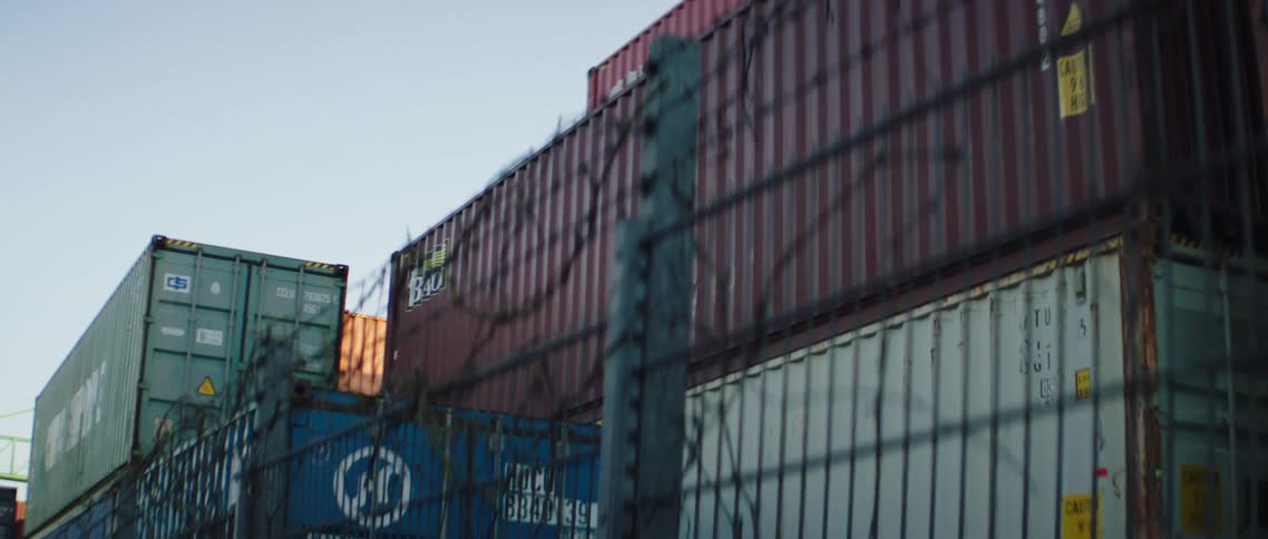 Several shipping containers are stored behind a fence