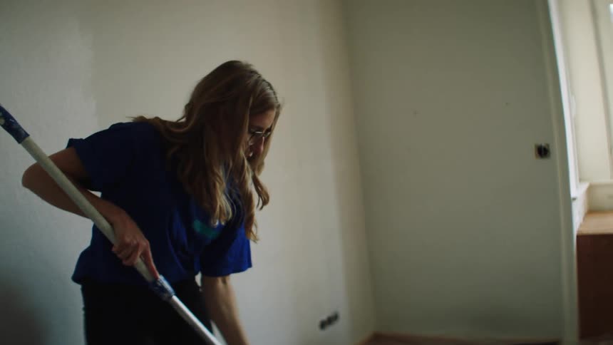 A woman dips a roller in paint to paint a room