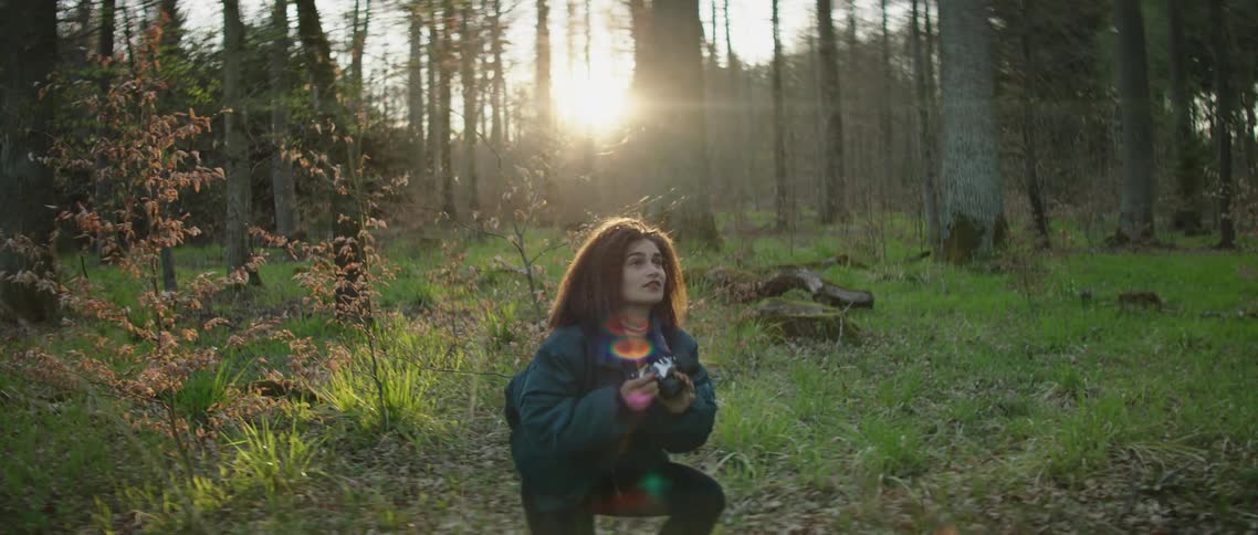Women kneels on the ground as she takes a photo with a camera in the forest