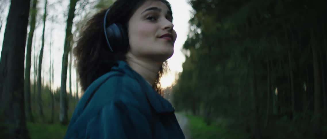 A woman in a forest spins in circles as she listens to music
