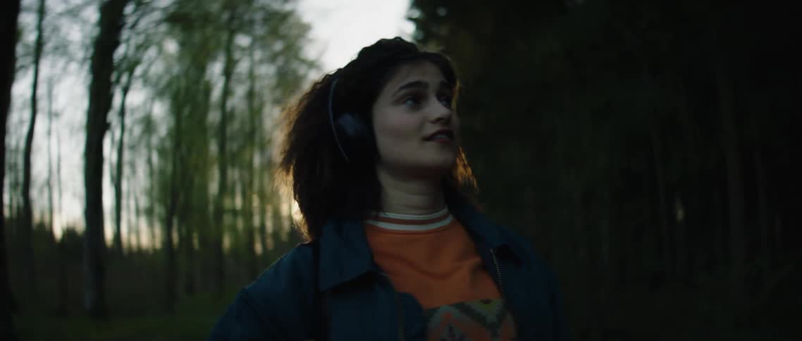 A woman walks around listening to her headphones on the trail