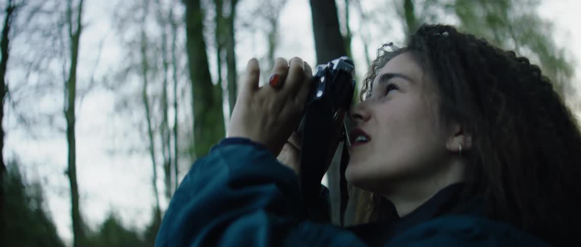 A woman looks up taking photographs in the forest
