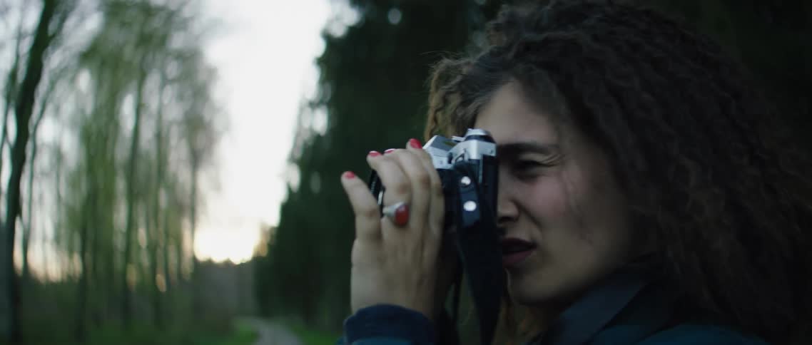 Female photographer takes pictures in a dirt path surrounded by trees at sunset