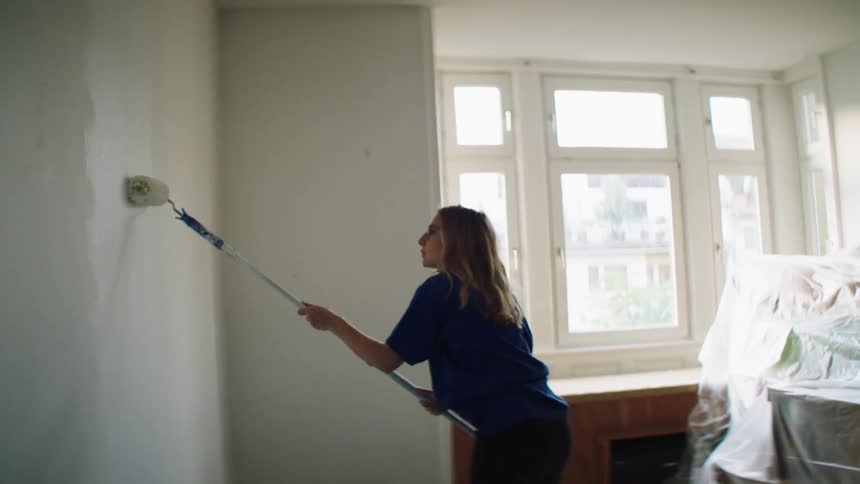 A young white woman paints a room in a living space