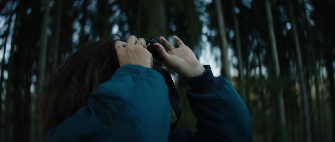 Woman stands in woods focusing camera upward