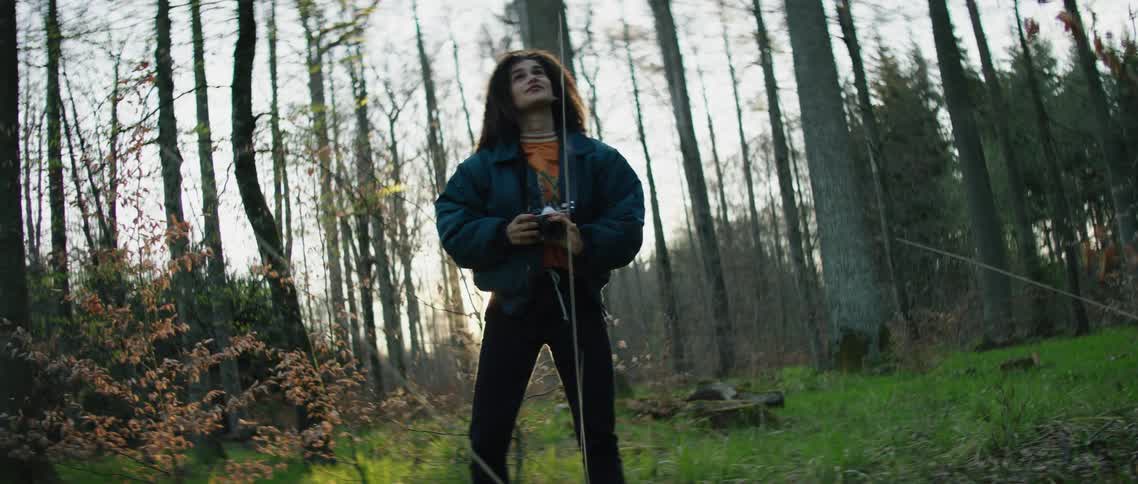 A hispanic woman takes a picture in the woods and then walks away