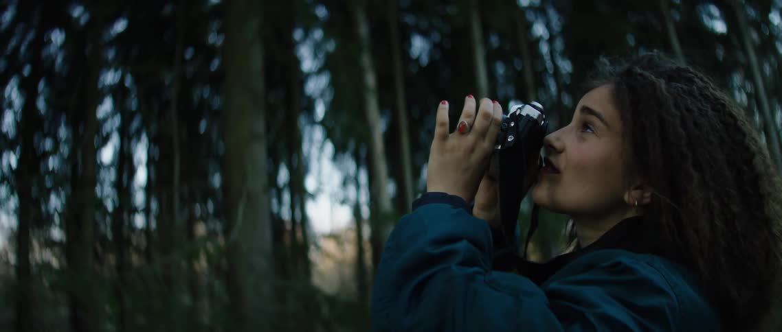 A woman in a forest with a camera taking pictures