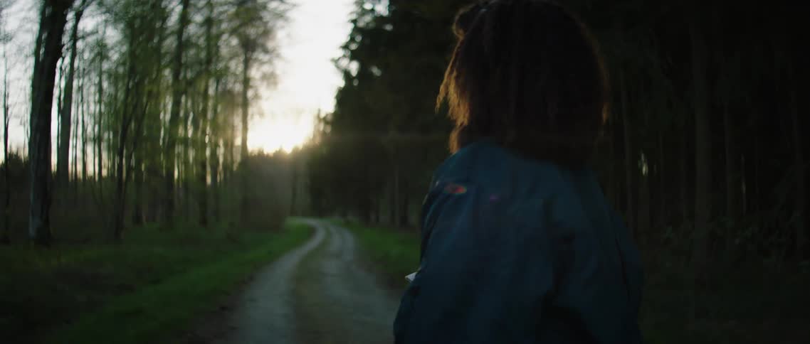 Woman checks phone and looks around walking on country road in middle of woods at sunset