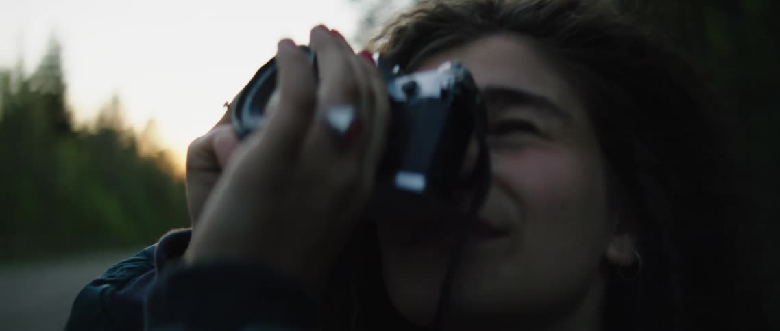 A hispanic woman raises a camera to take a picture while out in the woods