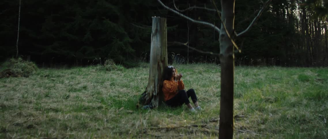Young woman sitting against tree in clearing lights cigarette