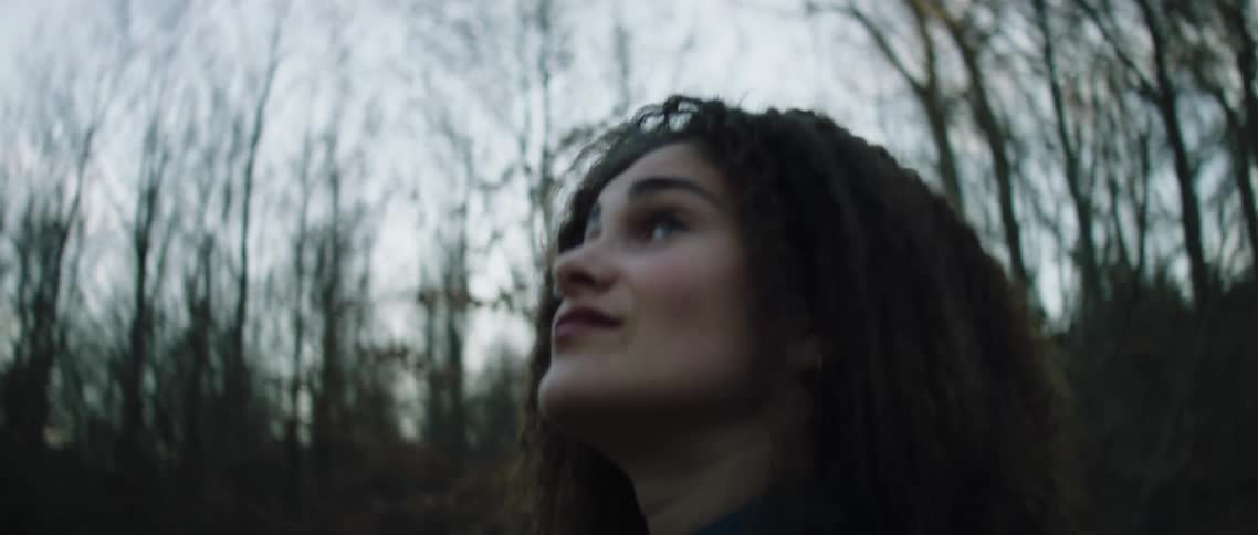 A woman in a forest looks around