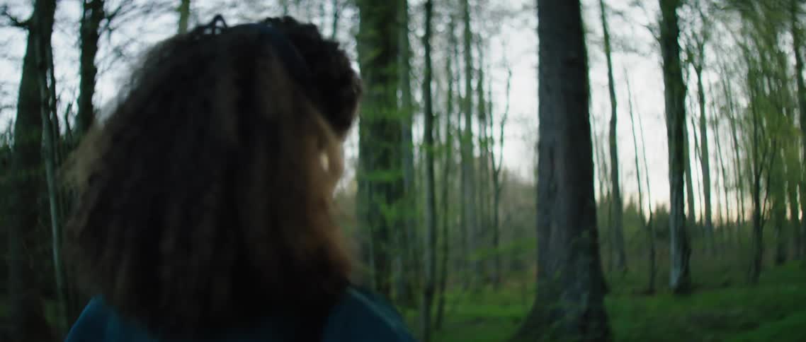 A woman listens to music on her smartphone and dances around a forest