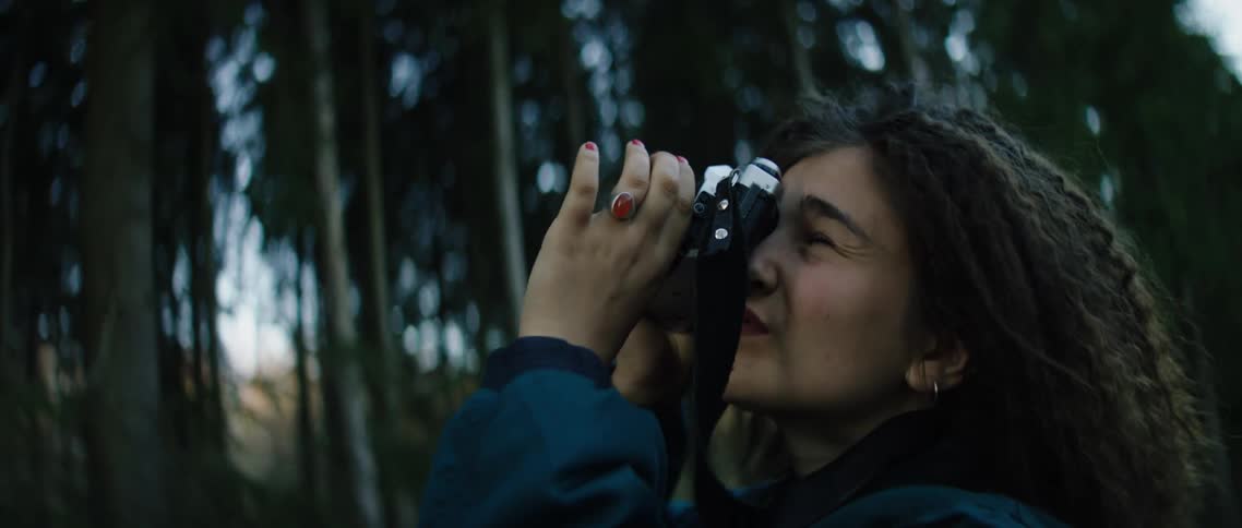 A woman holds up a camera in the forest